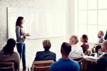 Formatrice che spiega alla lavagna il corso di accrescimento professionale e gruppo di persone che ascoltano in circolo